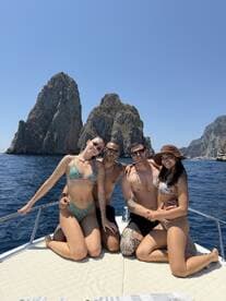 A joyful group of friends poses on the deck of a boat against a stunning rocky backdrop, perfect for summer adventures and beach celebrations.