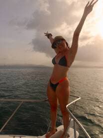 A joyful woman poses on the deck of a boat, celebrating under the clouds — a perfect moment for fun and adventure on the water.