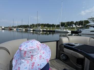 A child wearing a playful seahorse hat enjoys a scenic view from a boat at the marina, surrounded by various vessels — a perfect family outing on the water.