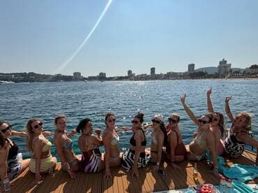 A lively group of friends enjoys a sunny day on a yacht, celebrating with smiles and fun by the water — perfect for a beach party or girls' getaway.