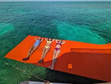 Three friends relax on a vibrant floating mat in crystal-clear waters, enjoying a perfect day of sunbathing and fun on the water.