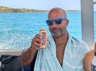 A man enjoys a refreshing drink while relaxing on a boat, surrounded by beautiful turquoise waters — perfect for a day of leisure and celebration.