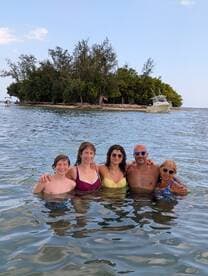 A joyful group of family members enjoys a refreshing swim near a picturesque island, capturing the essence of a perfect beach day.