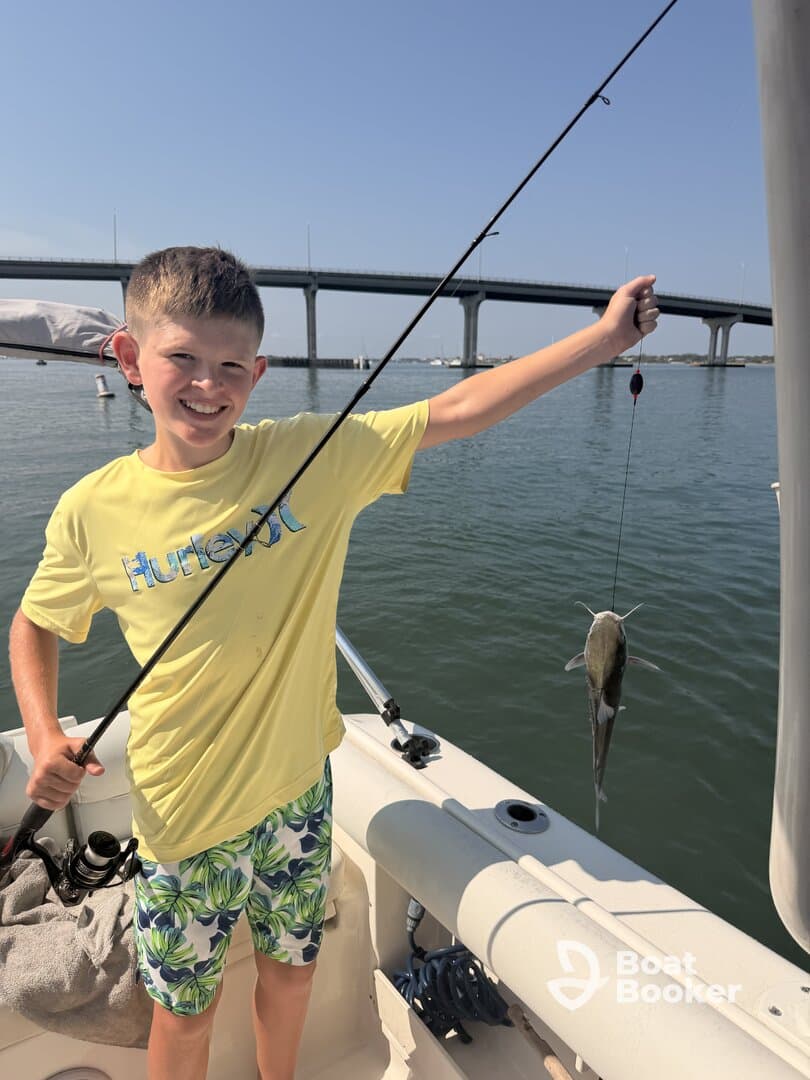 A young boy proudly displays his catch while fishing from a boat, capturing the joy of a family fishing trip on the water.