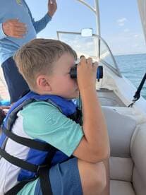 A young boy uses binoculars to explore the surroundings while on a boat, capturing the spirit of adventure and discovery on the water.