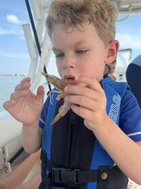 A young boy curiously examines a shrimp while on a boat, showcasing a delightful moment of marine exploration — perfect for family adventures on the water.
