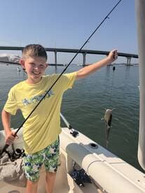 A young boy proudly displays his catch while fishing from a boat, capturing the joy of a family fishing trip on the water.