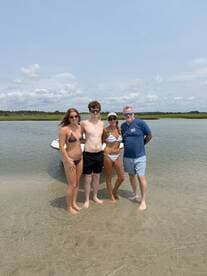A cheerful group of friends enjoys a sunny day at the beach, standing in shallow water next to their boat — perfect for summer fun and memorable outings.