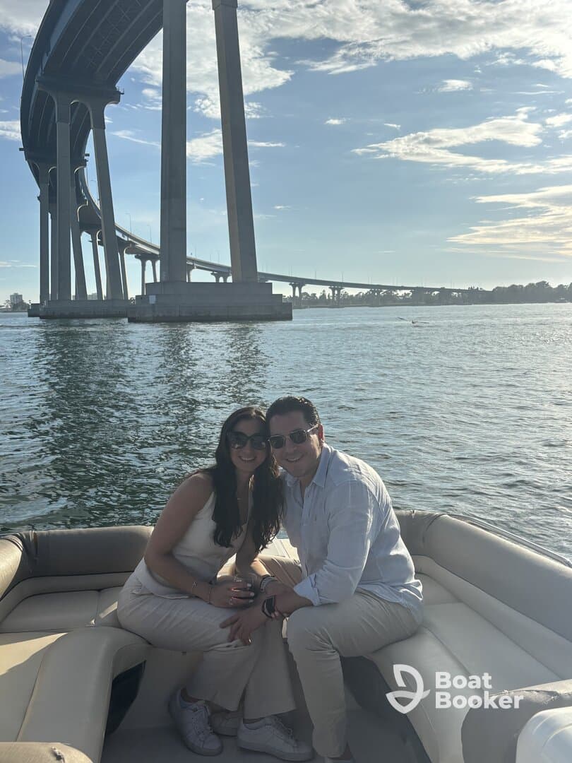A couple enjoys a sunny day on a boat, smiling together with a scenic bridge in the background — perfect for romantic outings or special celebrations on the water.