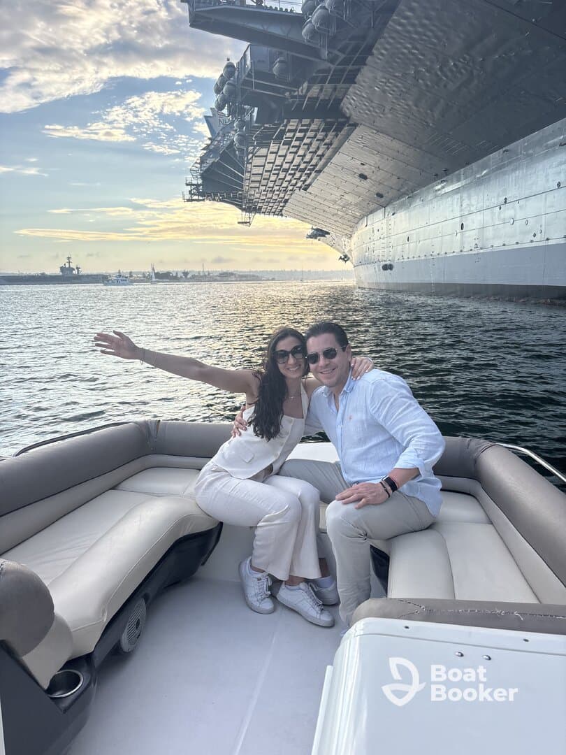 A couple enjoys a romantic moment on a boat with a military ship in the background, perfect for sunset celebrations and memorable outings on the water.