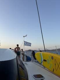 Guests enjoy a sailing experience in Greece, with a beautiful view of the sea and a Greek flag waving in the breeze — perfect for adventure seekers and sailing enthusiasts.