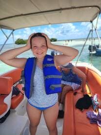 A joyful girl wearing a life jacket poses on a boat, ready for a fun day on the water with friends and family.