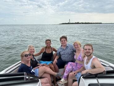 A cheerful group of friends enjoys a day on the water, capturing memories aboard their boat with a scenic lighthouse in the background.
