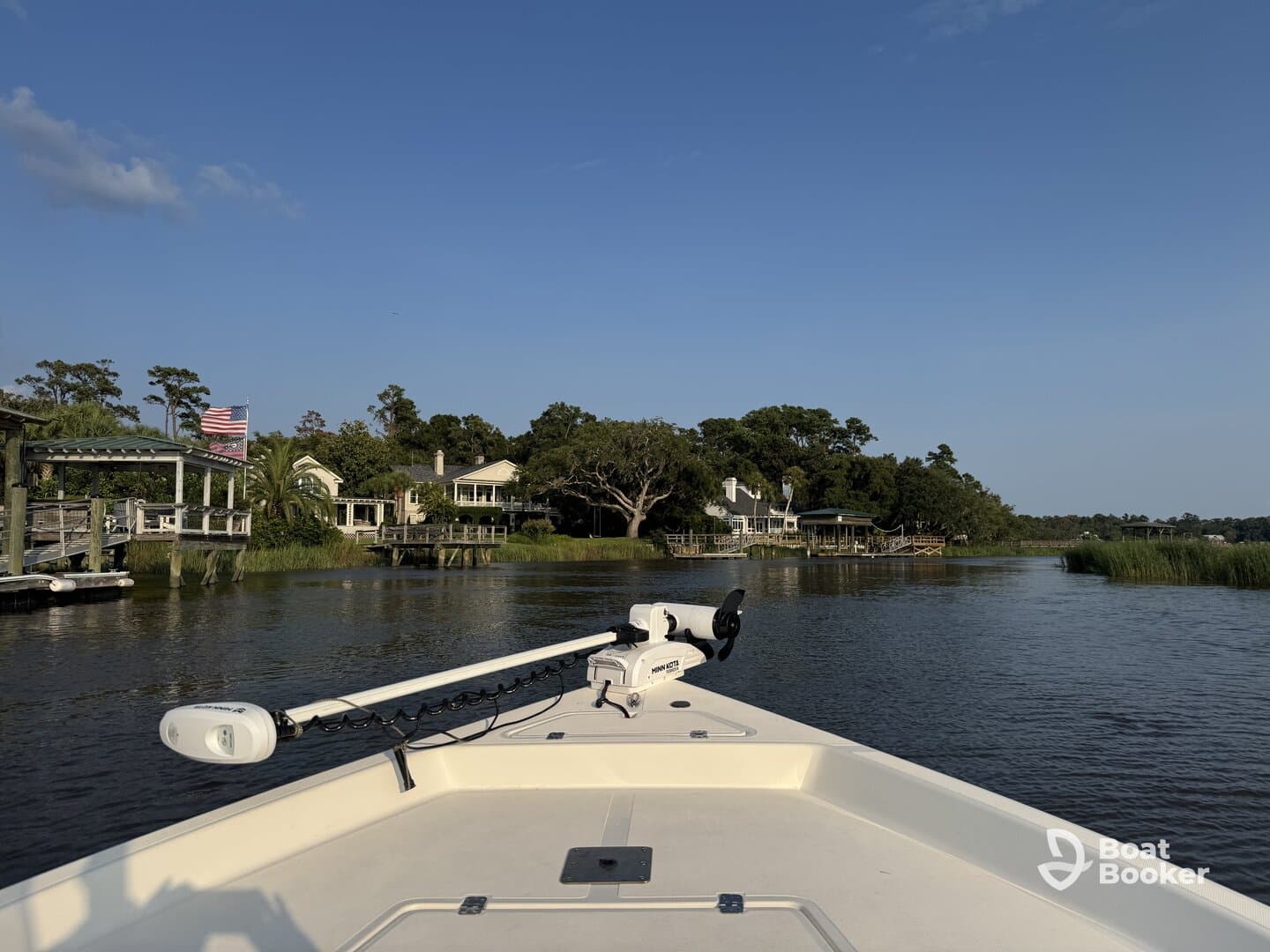 A scenic view from the front of a boat navigating through calm waters, showcasing beautiful waterfront homes and lush greenery along the shoreline.