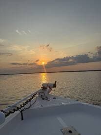 A serene sunset view from the bow of a boat, showcasing the tranquil waters and vibrant sky — perfect for evening cruises.