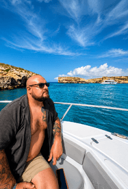 A man enjoys the stunning ocean views from the deck of a boat, surrounded by beautiful rocky cliffs and clear blue waters — a perfect moment for relaxation on the water.