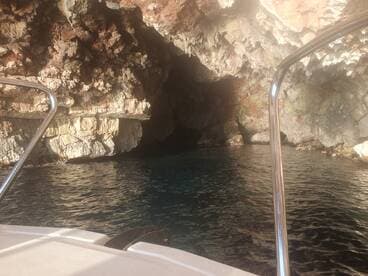 A stunning view of a rocky cave entrance from the deck of a boat, showcasing the serene waters and natural beauty of the surroundings.