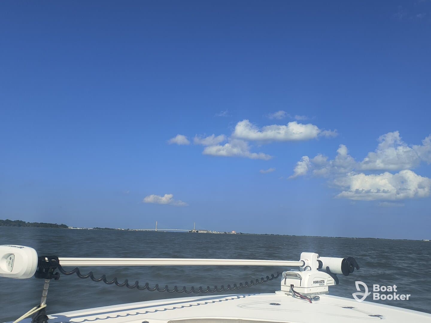 A clear view from the bow of a boat cruising through calm waters, showcasing the serene blue sky and distant bridge — perfect for a day on the water.