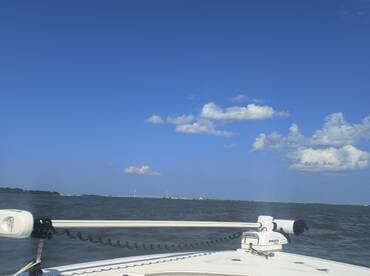 A clear view from the bow of a boat cruising through calm waters, showcasing the serene blue sky and distant bridge — perfect for a day on the water.