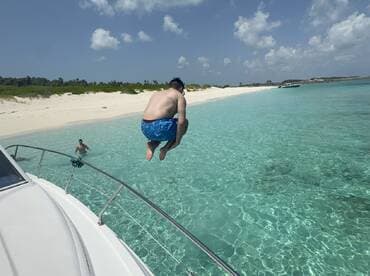 A thrilling moment captured as a person jumps off the boat into the crystal-clear waters, with a beautiful beach backdrop — perfect for summer adventures and water fun.