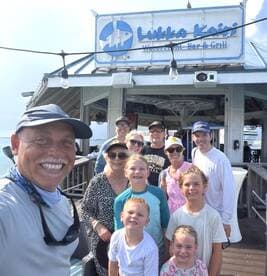 A cheerful group of family and friends poses for a selfie at Lukka Kairi Waterfront Bar & Grill, capturing a memorable moment by the water.