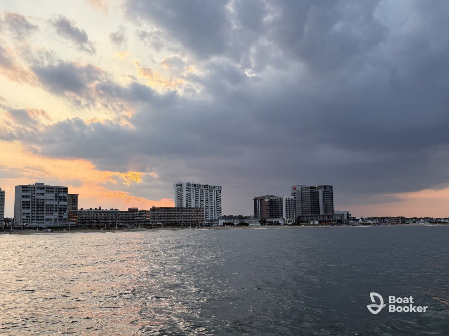 A scenic view of a waterfront with buildings and a cloudy sky at sunset, creating a tranquil atmosphere.