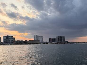 A scenic view of a waterfront with buildings and a cloudy sky at sunset, creating a tranquil atmosphere.