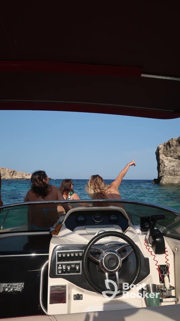 A group of friends enjoys a scenic boat ride, pointing towards a stunning rock formation along the coastline — perfect for adventure seekers and nature lovers.