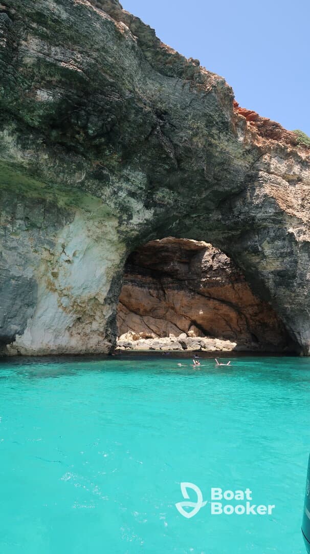 Swimmers enjoy the stunning turquoise waters near a natural cave, creating a picturesque backdrop for a memorable boating adventure.