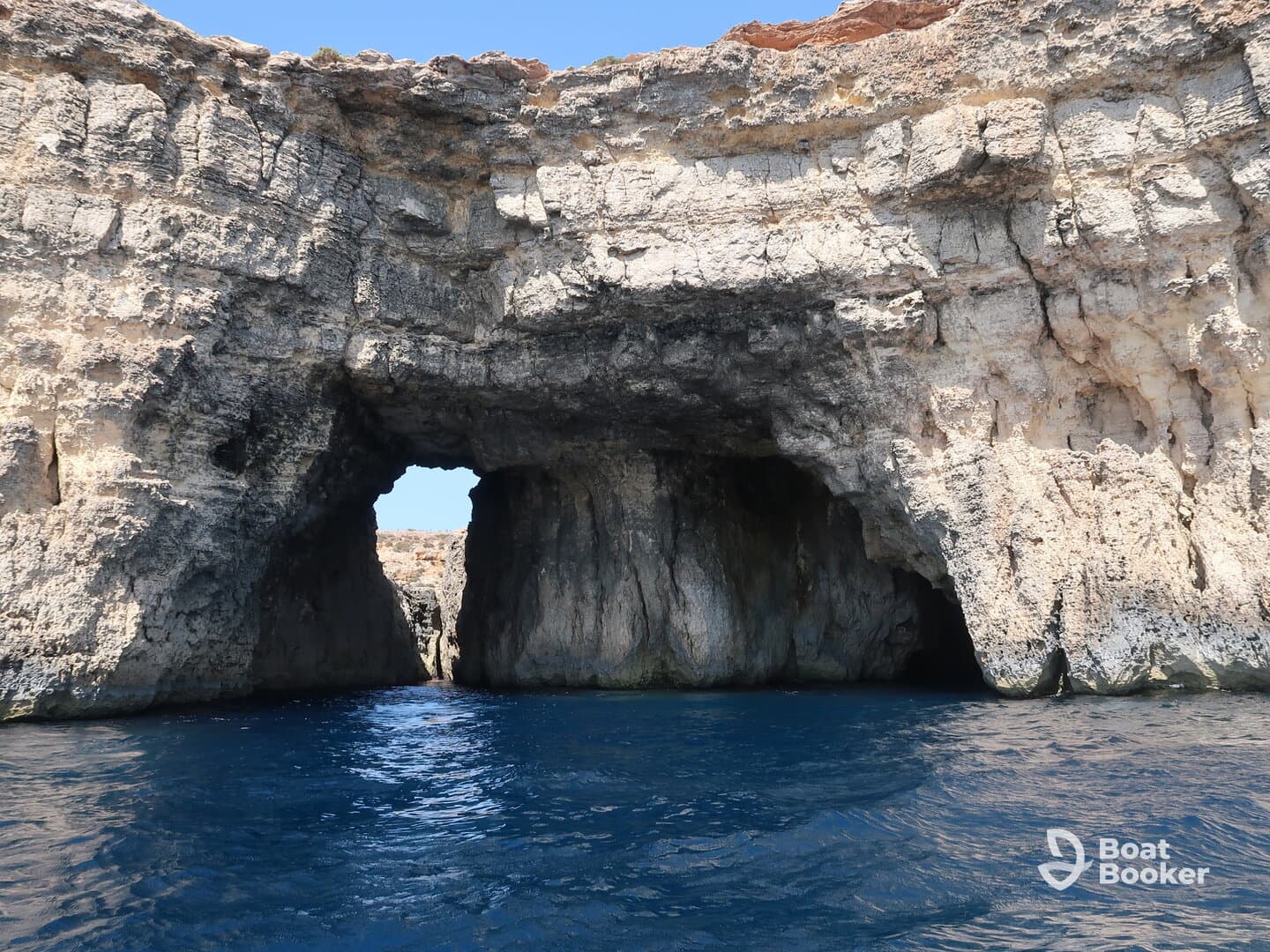 A stunning view of a natural rock formation with an arch, showcasing the beautiful coastline and clear blue waters — a perfect highlight for boating adventures.