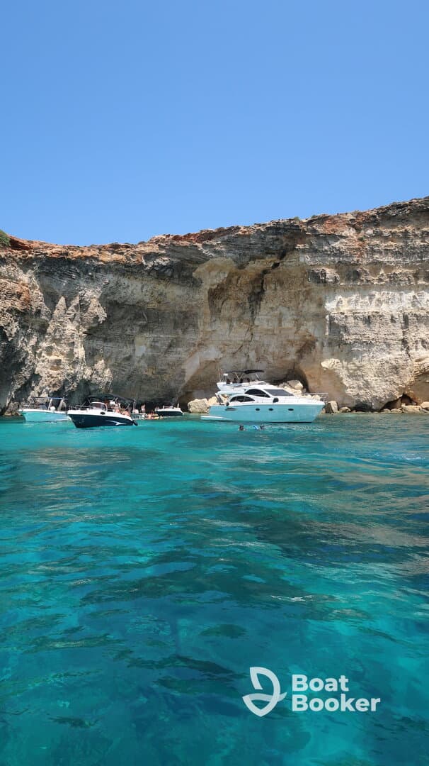 A picturesque scene featuring several boats anchored near a stunning rocky coastline, with people enjoying the clear turquoise waters — perfect for a summer getaway.
