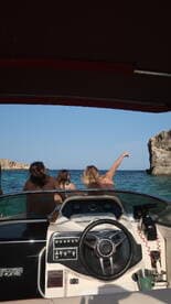 A group of friends enjoys a scenic boat ride, pointing towards a stunning rock formation along the coastline — perfect for adventure seekers and nature lovers.