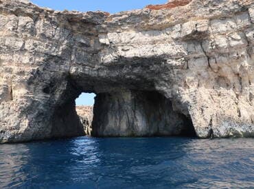 A stunning view of a natural rock formation with an arch, showcasing the beautiful coastline and clear blue waters — a perfect highlight for boating adventures.