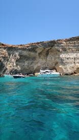 A picturesque scene featuring several boats anchored near a stunning rocky coastline, with people enjoying the clear turquoise waters — perfect for a summer getaway.