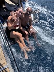 A couple enjoys a refreshing moment on the side of a boat, sipping drinks and splashing their feet in the water — a perfect snapshot of relaxation and fun on the water.