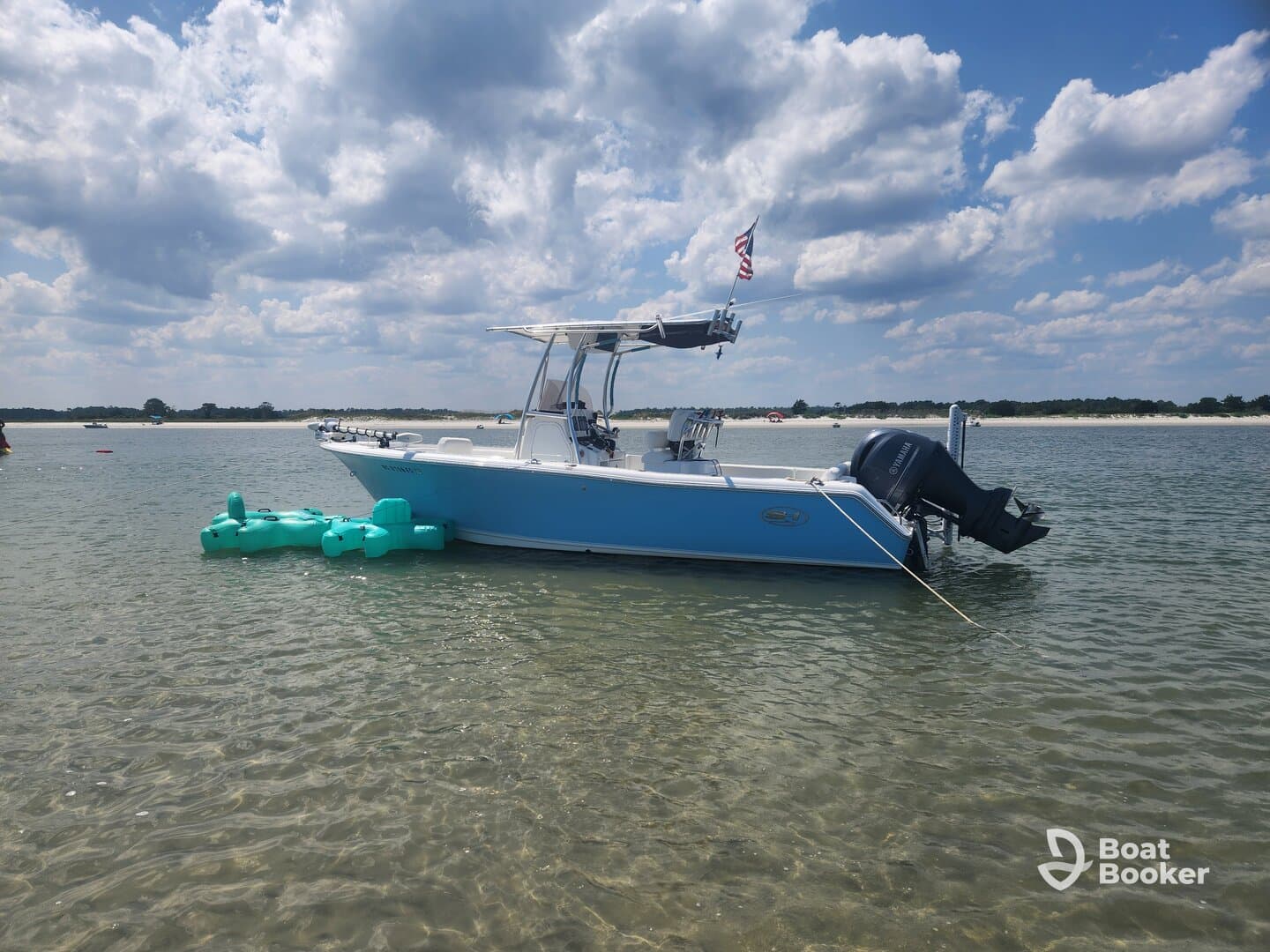 A sleek speedboat anchored in shallow waters, showcasing its vibrant blue hull against a backdrop of fluffy clouds and a sandy shoreline.