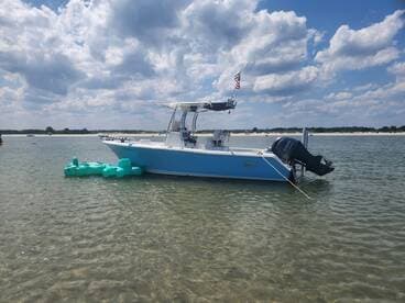 A sleek speedboat anchored in shallow waters, showcasing its vibrant blue hull against a backdrop of fluffy clouds and a sandy shoreline.
