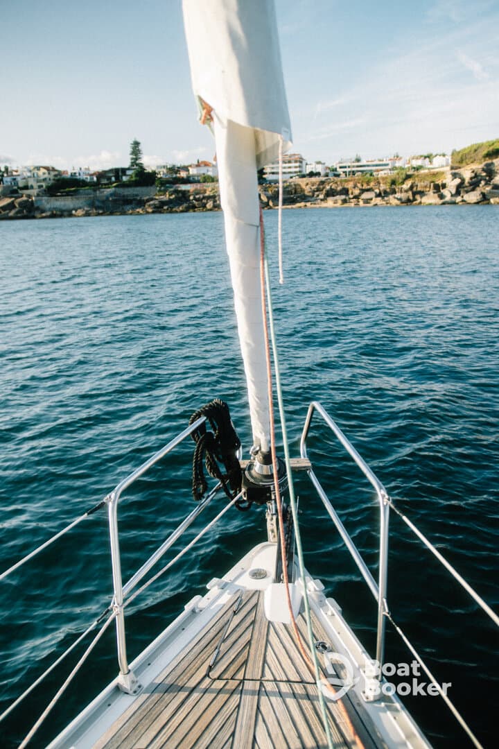 A stunning view from the bow of a sailboat, showcasing the vessel's sleek design against a backdrop of calm waters and coastal scenery.