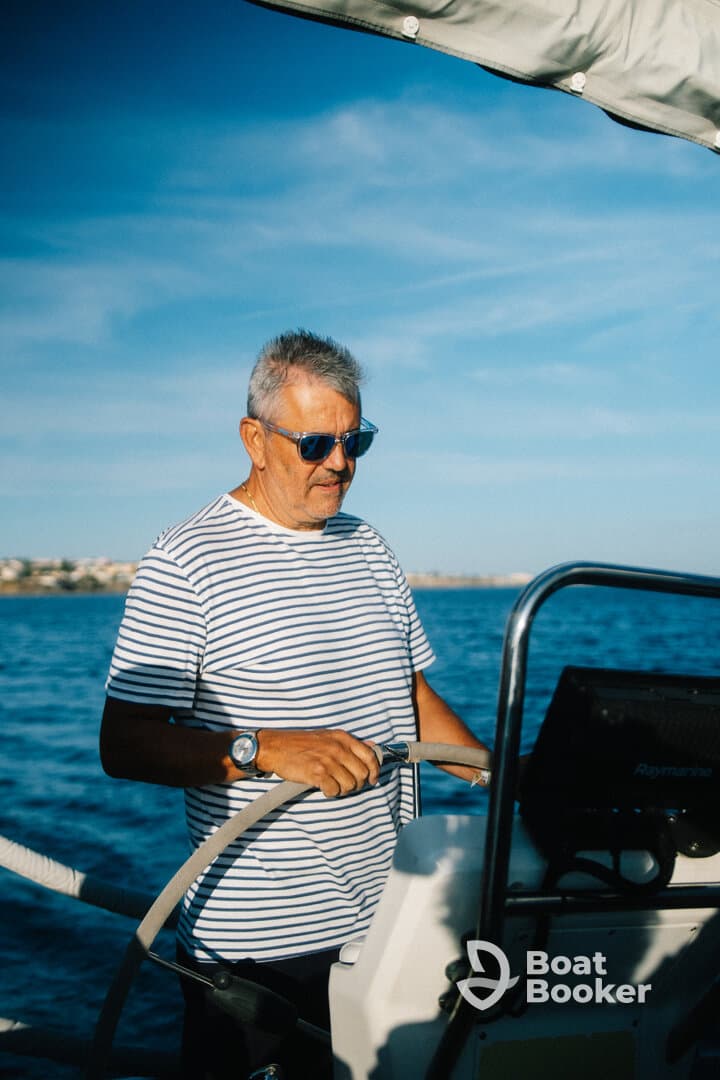 A skilled sailor navigates the waters from the helm, showcasing the joy of sailing under a clear blue sky.