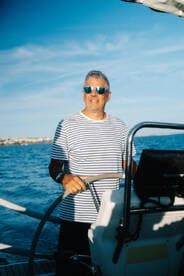 A confident captain navigates the waters while steering the helm of a sailboat, showcasing the joy of sailing adventures on the open sea.