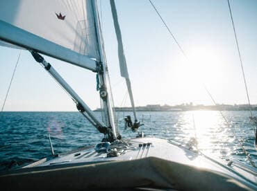 A stunning view from the deck of a sailboat, capturing the serene waters and the sun reflecting off the surface — perfect for sailing enthusiasts and sunset lovers.