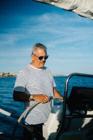 A skilled sailor navigates the waters from the helm, showcasing the joy of sailing under a clear blue sky.
