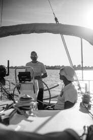 Two crew members aboard a sailboat engage in conversation as they navigate the waters, capturing the essence of sailing adventures.