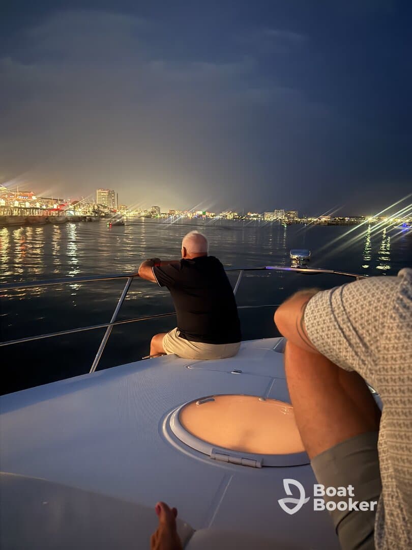 Two guests enjoy a serene evening on a boat, gazing at the vibrant city lights reflecting on the water — a perfect setting for nighttime cruises.
