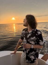 A man enjoys a sunset view on a boat, holding a drink and taking in the serene waterscape — perfect for romantic evenings or relaxing outings.