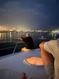 Two guests enjoy a serene evening on a boat, gazing at the vibrant city lights reflecting on the water — a perfect setting for nighttime cruises.