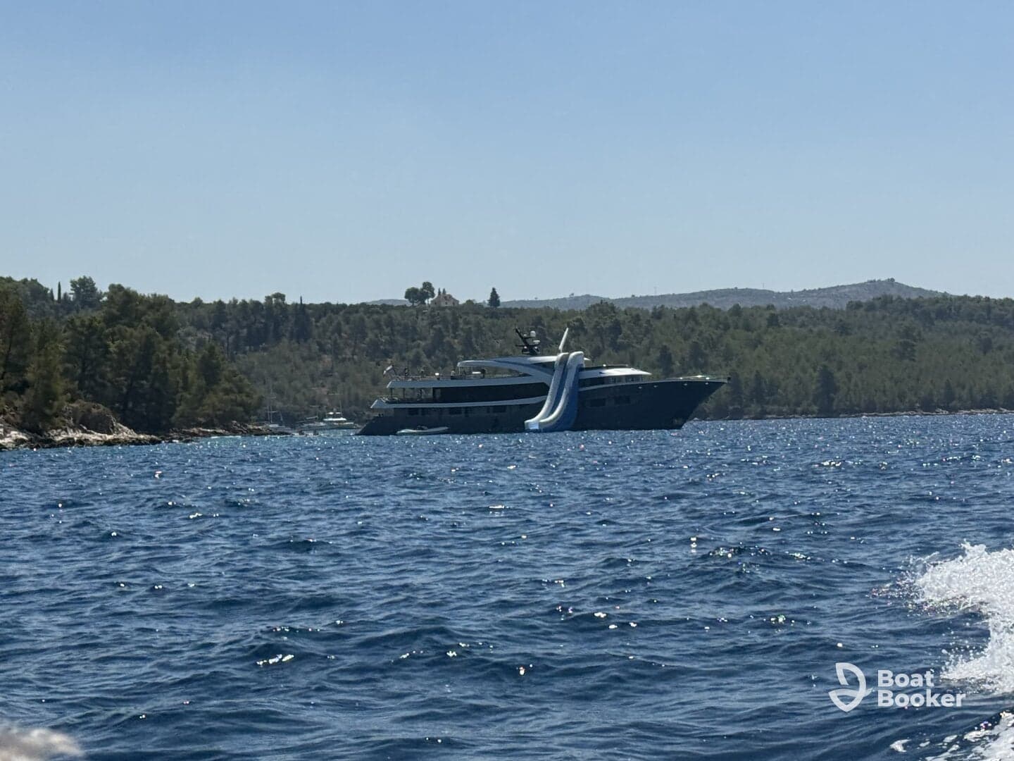 A stunning yacht with water slides is anchored in a serene bay, surrounded by lush greenery — perfect for luxury getaways and family fun on the water.