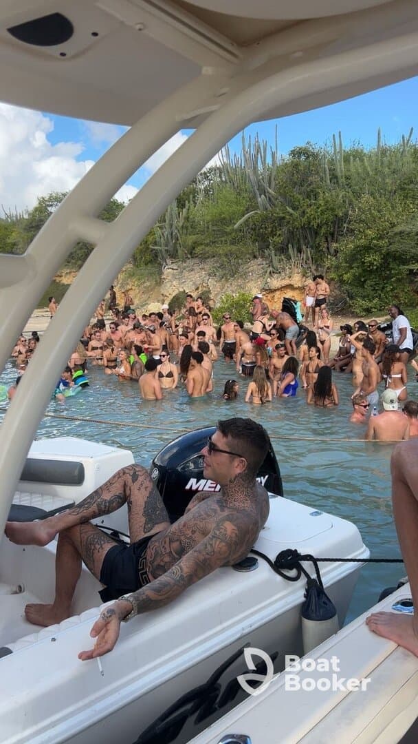 A lively beach party scene with a large group of people enjoying the water, while one individual relaxes on the boat — perfect for summer fun and social gatherings.