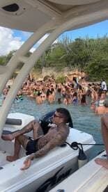A lively beach party scene with a large group of people enjoying the water, while one individual relaxes on the boat — perfect for summer fun and social gatherings.
