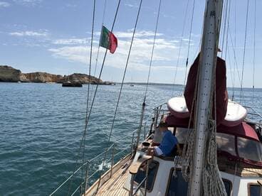 A child enjoys the view from a sailing boat, with stunning coastal cliffs in the background — a perfect moment of adventure on the water.